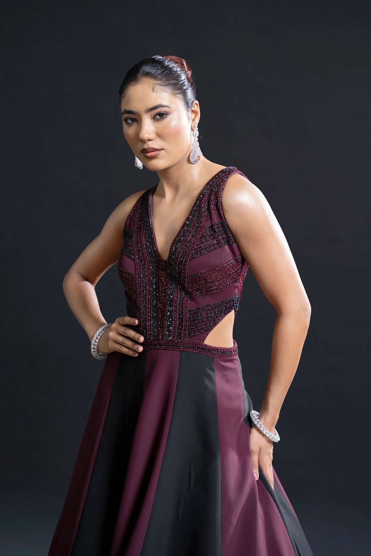 Woman wearing a burgundy evening gown with cut-out design on a dark background