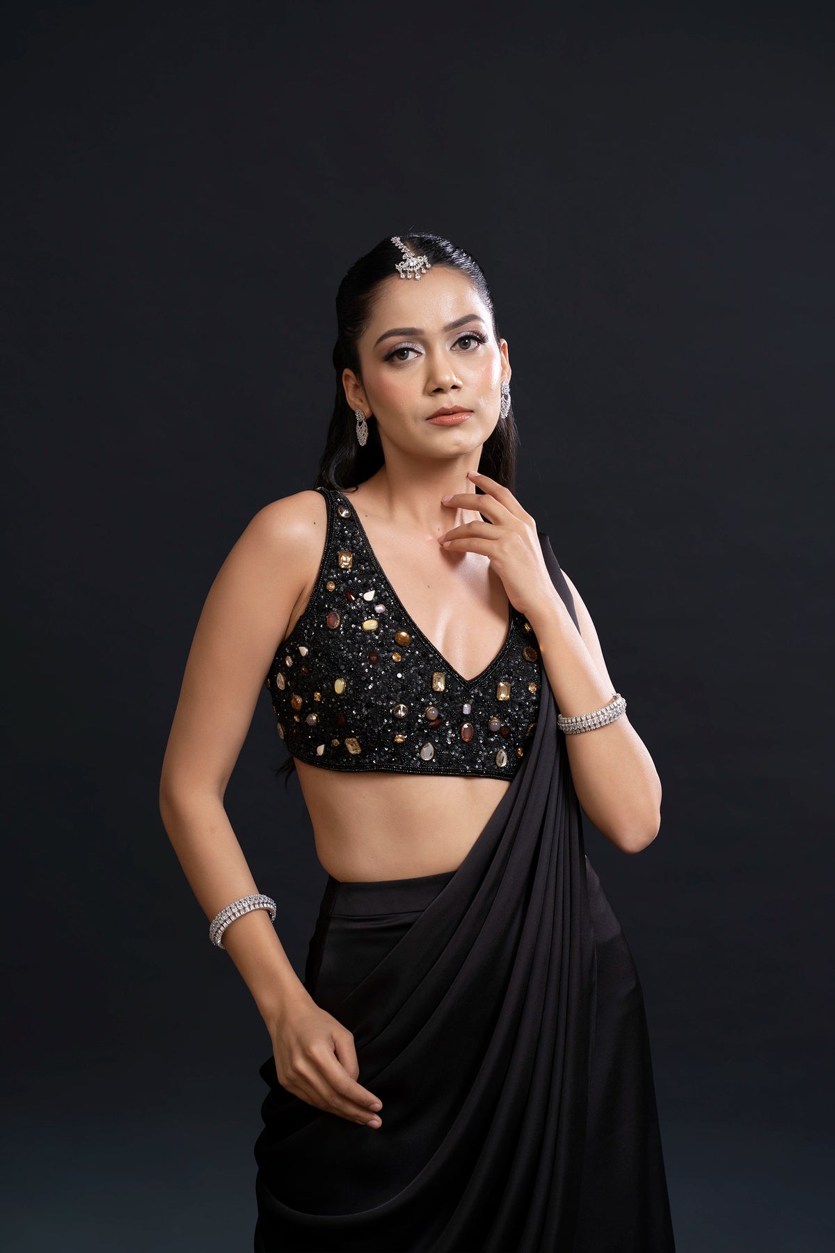 Woman wearing a black saree with gold detailing against a dark background