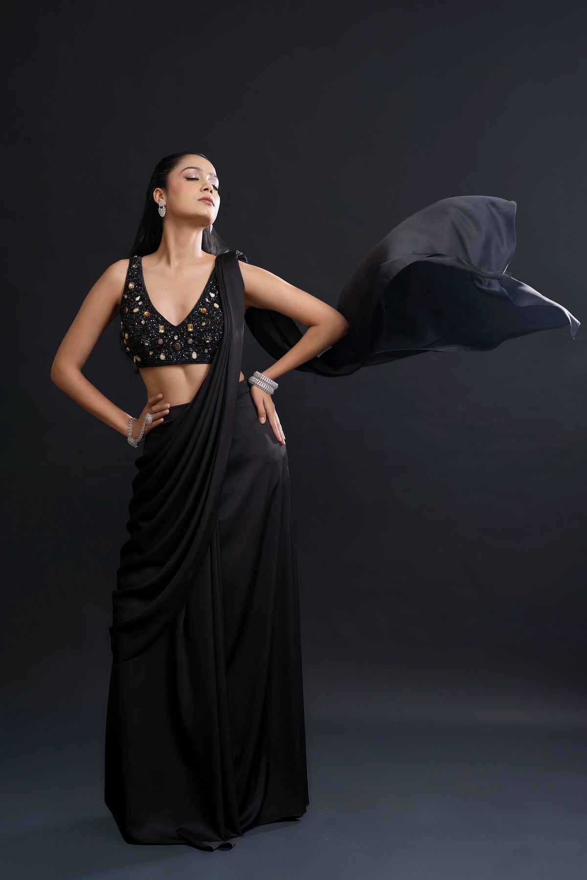 Woman in a black saree with a draped fabric against a dark background